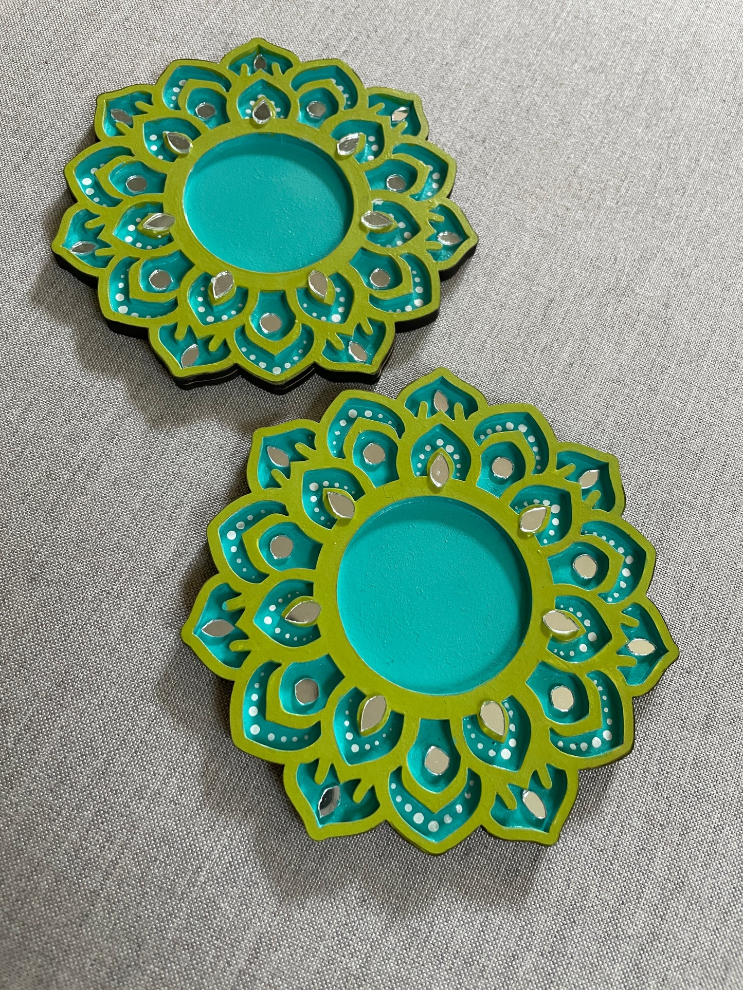 Two decorative circular plates with intricate green and turquoise patterns on a gray fabric background.